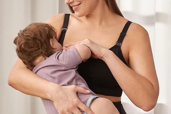 A smiling woman stands upright, holding her infant child. The newborn feeding guide help this moment.
