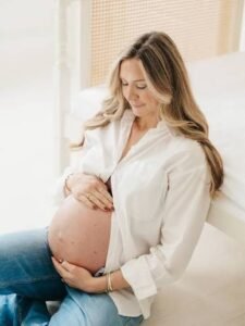 A happy, glowing pregnant blonde woman smiling and holding her belly, featured on the NewMomChoice free pregnancy week calculator.