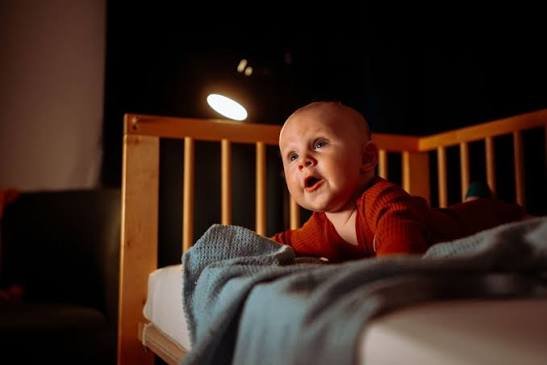 Wide-awake infant in a wooden crib illustrating a newborn won't sleep at night during tummy time.