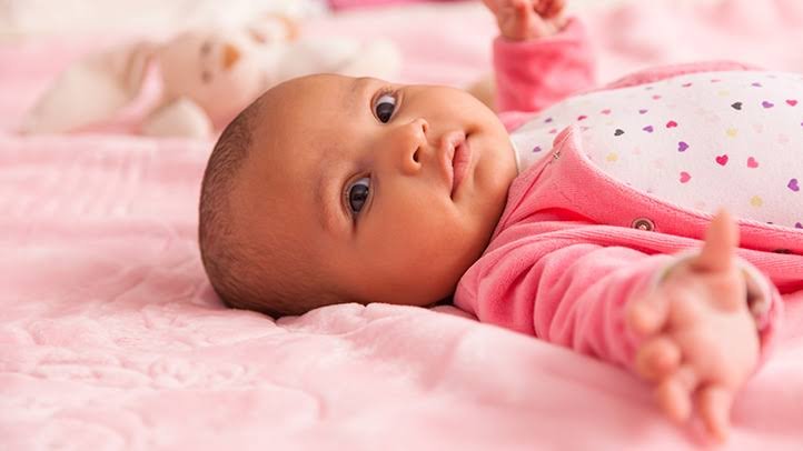 Awake baby girl lying on a pink blanket, representing an optimal newborn sleep schedule week by week.