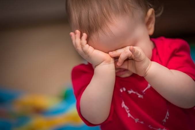 Newborn Sleep Cues: A close-up shot of a young baby rubbing their eyes with both hands, a common sign of tiredness.
