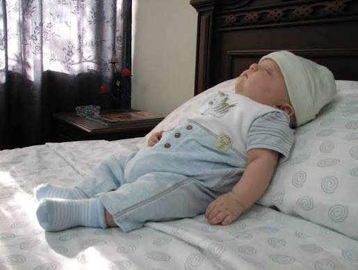 A baby sleeping propped up on a bed pillow, demonstrating a newborn sleep schedule by age for healthy infant rest.