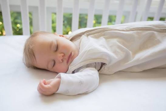 A baby sleeping soundly in a crib wearing a sleep sack, highlighting a consistent newborn nap schedule.