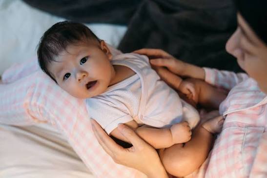 A mother holding a wide-awake baby on her lap, illustrating the common parenting dilemma: why does my newborn wake up when I put them down.