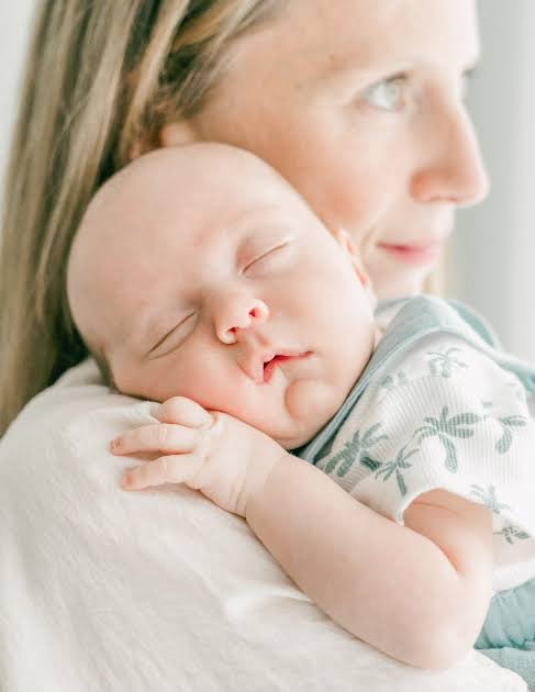 A mother holding a sleeping baby on her shoulder, addressing the question why does my newborn only sleep when held.
