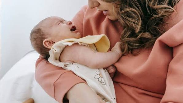 A mother cradling a crying newborn who baby fights naps while looking up at her.