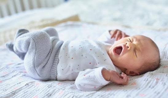 A yawning baby lying on a star-patterned blanket, showing sleep regression signs and demonstrating how to help with 4-month sleep regression.