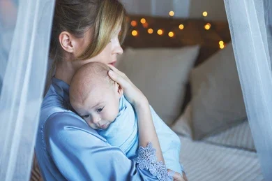 A mother holding a swaddled infant close to her shoulder, providing a visual context for understanding when to stop swaddling your baby.