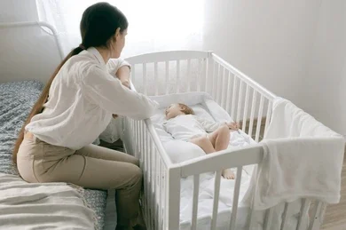 A mother watching her baby sleep flat on their back in a crib, demonstrating safe sleep for newborns guidelines.