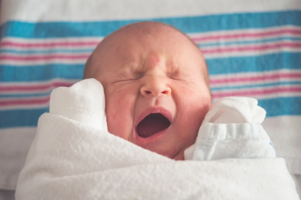 Swaddled overtired newborn yawning, illustrating early signs and what to do.