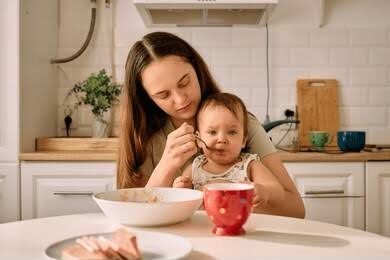 Newborn feeding cues shown by a baby sitting with a mother at a kitchen table during breakfast. 
